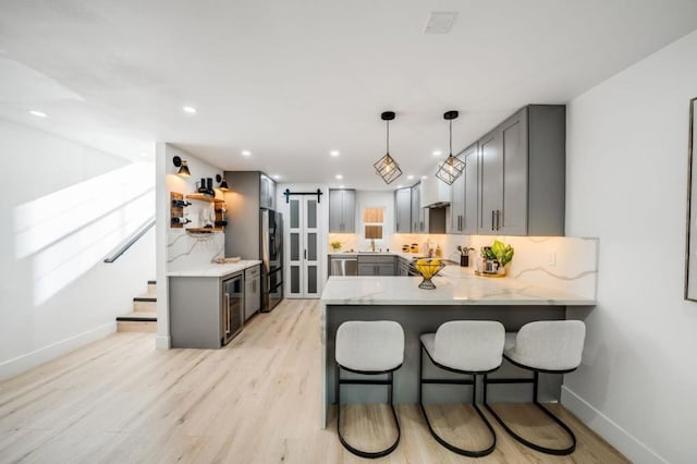 kitchen with kitchen peninsula, gray cabinetry, a barn door, decorative light fixtures, and fridge with ice dispenser