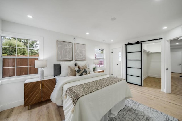 bedroom featuring a barn door, a walk in closet, light hardwood / wood-style flooring, and a closet