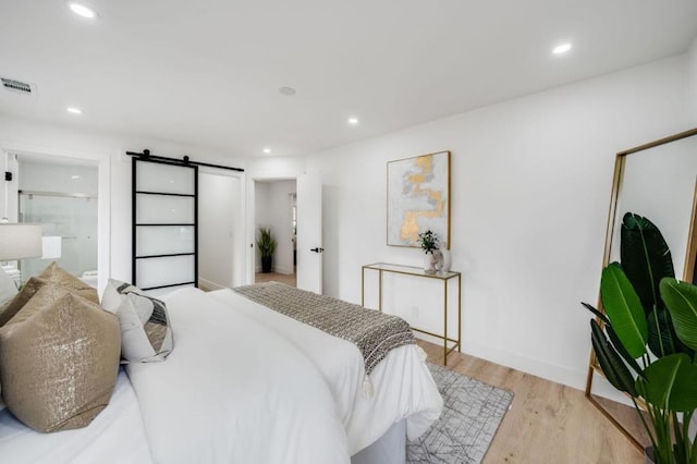 bedroom featuring a barn door, light wood-type flooring, and connected bathroom