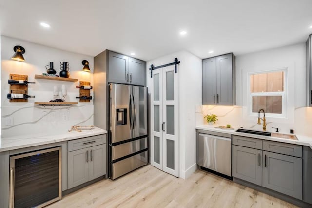 kitchen with gray cabinetry, sink, wine cooler, a barn door, and appliances with stainless steel finishes