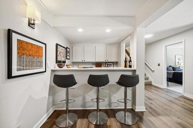 kitchen with white cabinetry, kitchen peninsula, a breakfast bar area, and light wood-type flooring