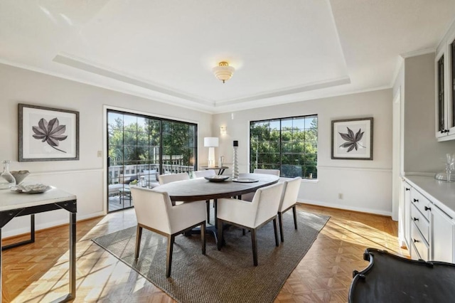 dining space with light parquet flooring, a healthy amount of sunlight, crown molding, and a tray ceiling