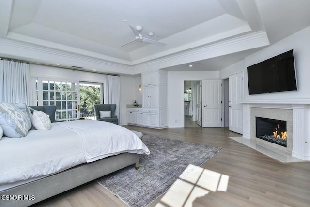 bedroom featuring a high end fireplace, a raised ceiling, ceiling fan, and wood-type flooring