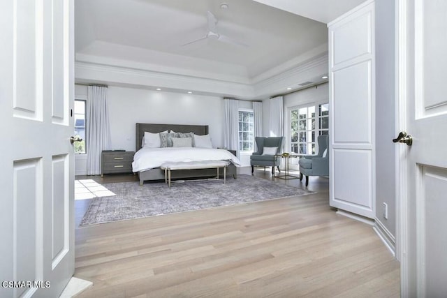 bedroom with light wood-type flooring, ceiling fan, and a tray ceiling