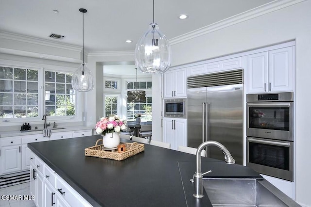 kitchen with built in appliances, sink, decorative light fixtures, and white cabinetry