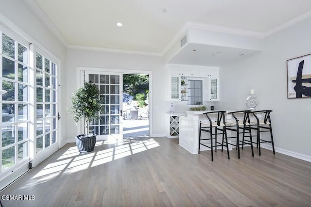 interior space with white cabinets, light hardwood / wood-style floors, a kitchen bar, and crown molding