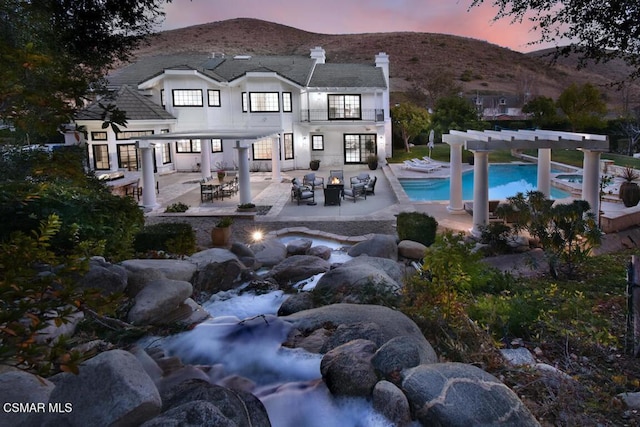 back house at dusk with a balcony, a patio, a mountain view, and an outdoor fire pit