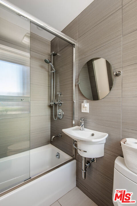 full bathroom with sink, tile patterned flooring, combined bath / shower with glass door, toilet, and tile walls