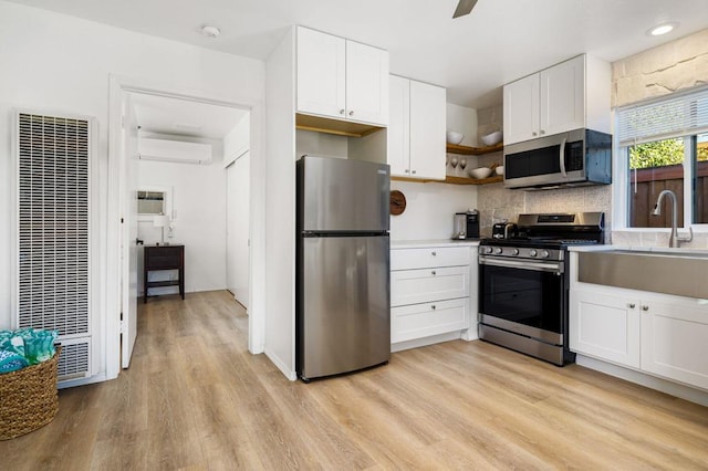 kitchen featuring appliances with stainless steel finishes, white cabinetry, light hardwood / wood-style floors, and an AC wall unit