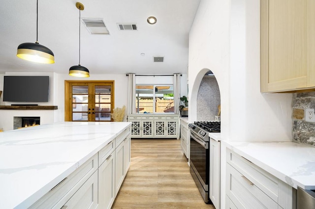 kitchen featuring light stone counters, stainless steel gas range oven, decorative backsplash, and hanging light fixtures