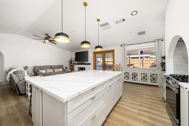 kitchen with stainless steel gas range, decorative light fixtures, lofted ceiling, a kitchen island, and white cabinets