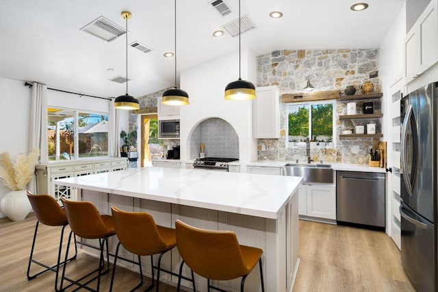 kitchen featuring pendant lighting, stainless steel appliances, lofted ceiling, white cabinetry, and sink