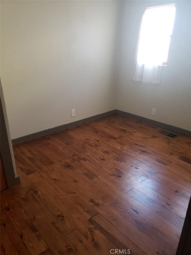 empty room with baseboards, visible vents, and dark wood-type flooring