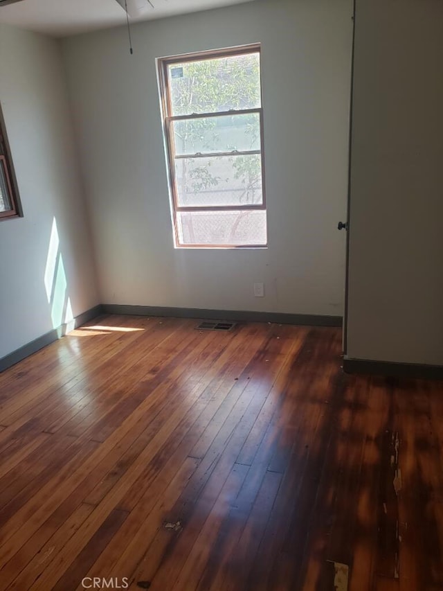 spare room featuring dark wood-style flooring, visible vents, and baseboards