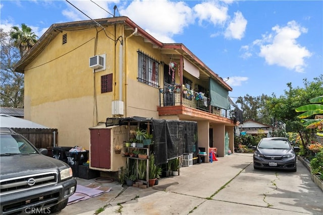 view of side of home featuring a balcony, an AC wall unit, and stucco siding