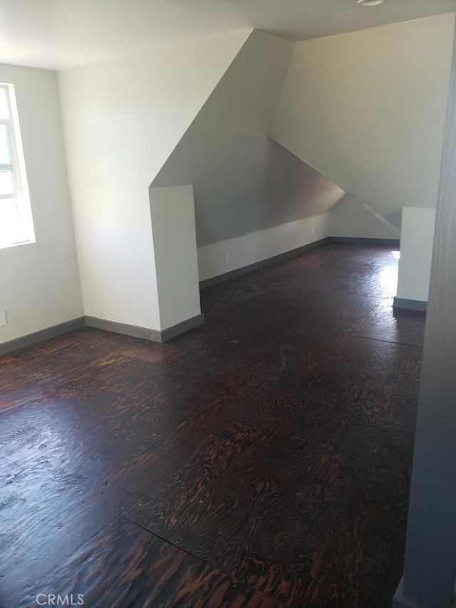 additional living space featuring baseboards, vaulted ceiling, and dark wood-style flooring