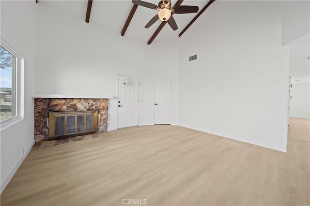 unfurnished living room featuring ceiling fan, high vaulted ceiling, beamed ceiling, a fireplace, and light hardwood / wood-style floors