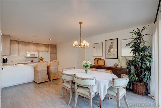 dining area with sink, a chandelier, and light wood-type flooring