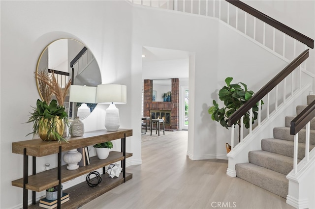 entrance foyer featuring a brick fireplace, a high ceiling, and light wood-type flooring