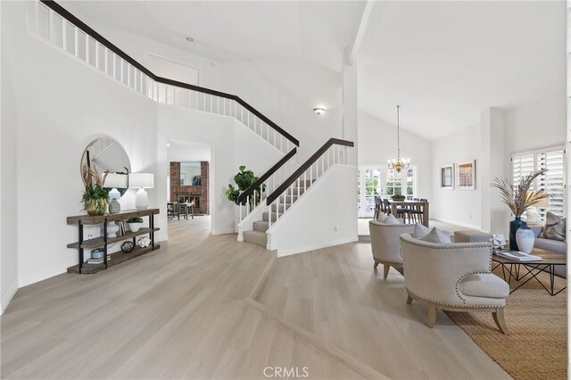 foyer entrance with a glass covered fireplace, stairway, wood finished floors, an inviting chandelier, and high vaulted ceiling