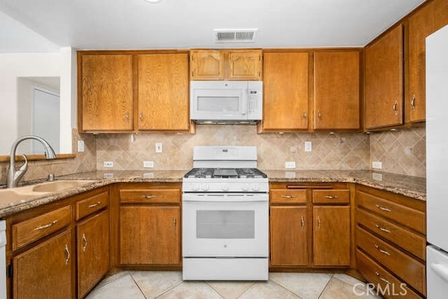 kitchen featuring light stone countertops, white appliances, tasteful backsplash, and sink