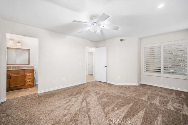 unfurnished bedroom featuring ceiling fan, light colored carpet, and ensuite bath