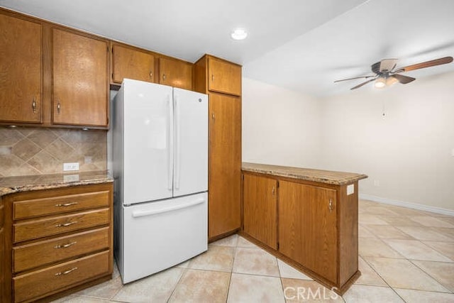 kitchen with ceiling fan, tasteful backsplash, light stone counters, white refrigerator, and kitchen peninsula