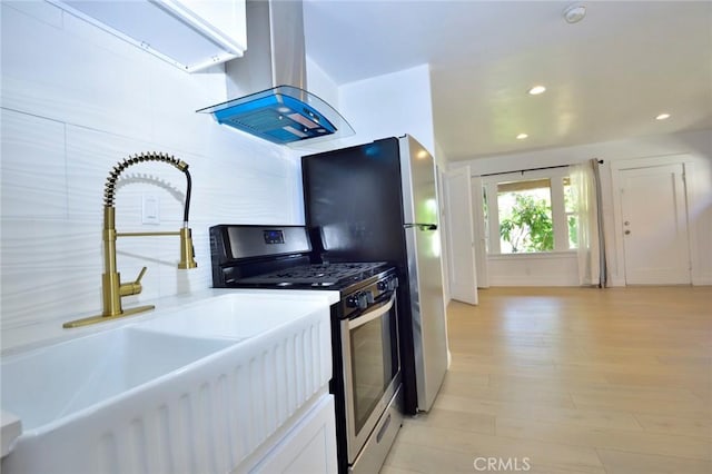 kitchen featuring stainless steel gas range oven, sink, light wood-type flooring, white cabinetry, and island exhaust hood