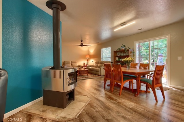 dining area with ceiling fan, a wood stove, a textured ceiling, and light hardwood / wood-style flooring