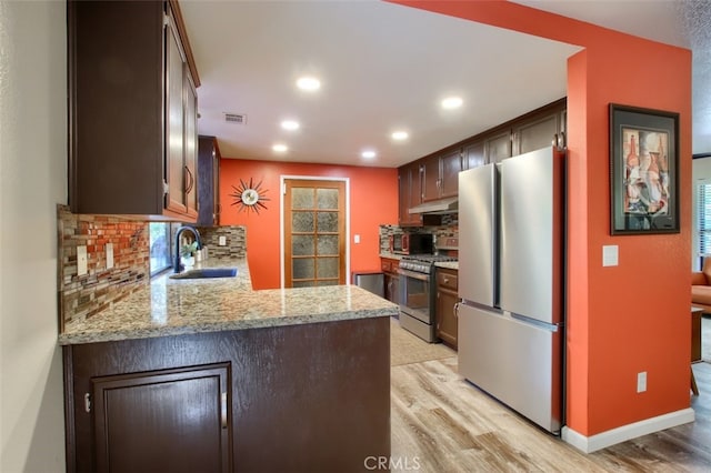 kitchen featuring kitchen peninsula, appliances with stainless steel finishes, decorative backsplash, light stone countertops, and sink