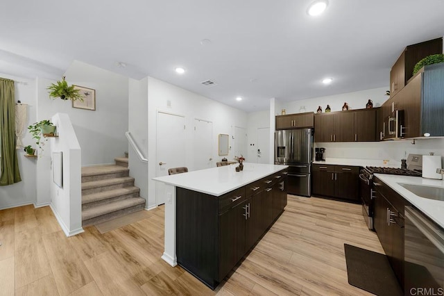 kitchen with light wood-type flooring, appliances with stainless steel finishes, dark brown cabinetry, and a kitchen island