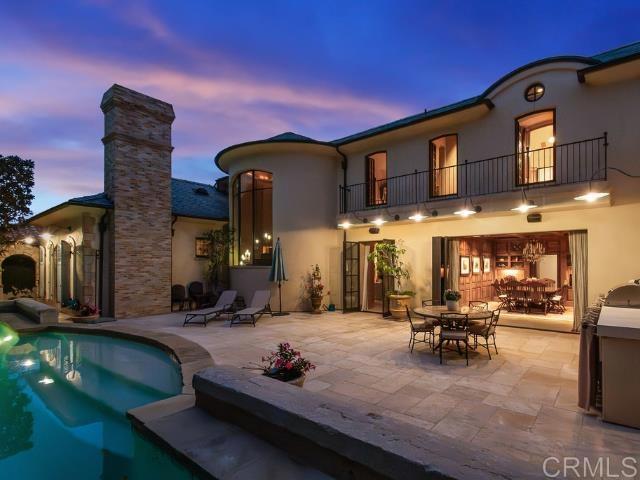 back house at dusk featuring a balcony and a patio area