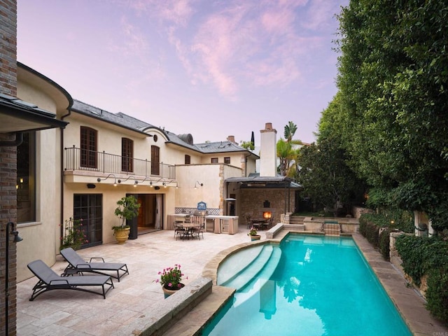 pool at dusk with a patio area and exterior fireplace