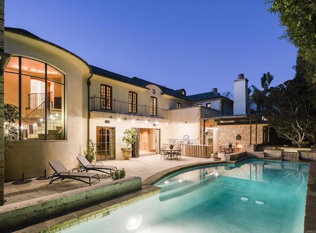 rear view of house with a chimney, stucco siding, a patio area, a balcony, and an outdoor pool