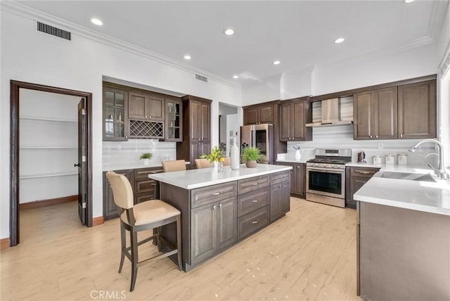 kitchen featuring sink, wall chimney exhaust hood, stainless steel appliances, a kitchen breakfast bar, and a kitchen island