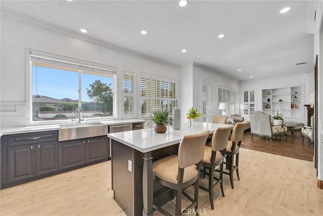 kitchen with ornamental molding, sink, light hardwood / wood-style floors, a kitchen island, and a breakfast bar area