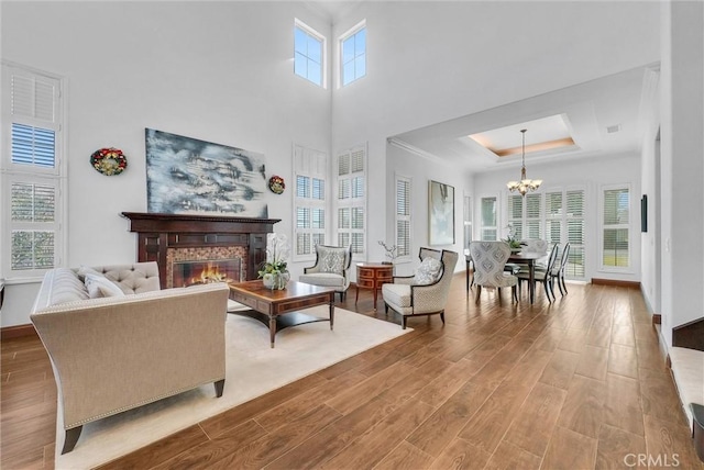 living room with a raised ceiling, a fireplace, a towering ceiling, and an inviting chandelier