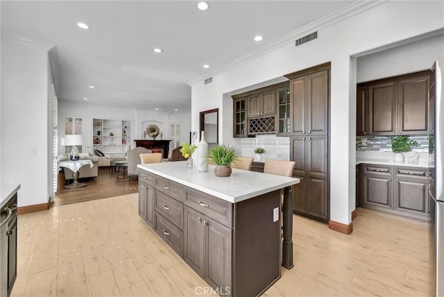 kitchen with decorative backsplash, dark brown cabinetry, crown molding, a center island, and light hardwood / wood-style floors