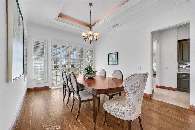 dining area with an inviting chandelier, a raised ceiling, and ornamental molding