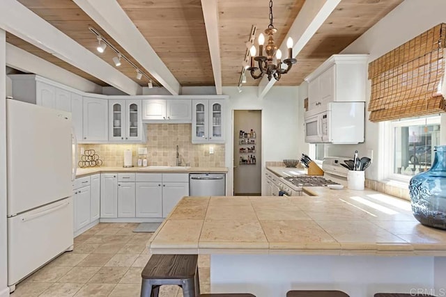 kitchen featuring white appliances, white cabinetry, beamed ceiling, hanging light fixtures, and kitchen peninsula