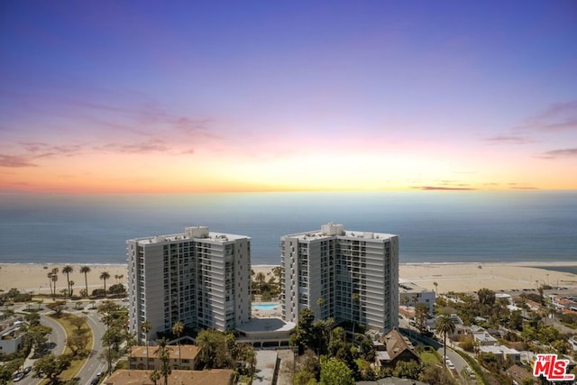 aerial view at dusk with a water view and a beach view