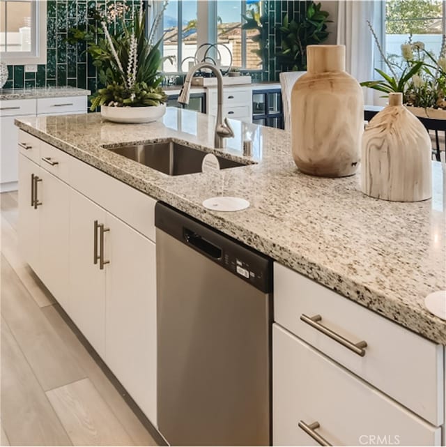 kitchen featuring stainless steel dishwasher, light stone counters, white cabinets, and sink