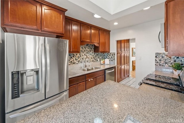 kitchen with appliances with stainless steel finishes, light tile patterned floors, light stone counters, sink, and backsplash