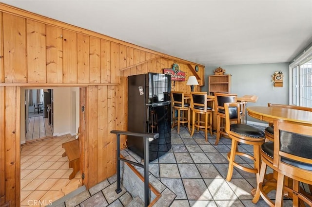 kitchen with black fridge, wood walls, and light tile patterned flooring