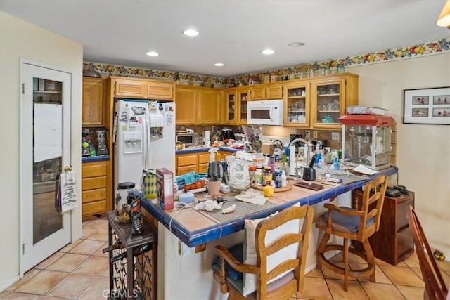 kitchen featuring a breakfast bar area, white appliances, light tile patterned flooring, and tile counters