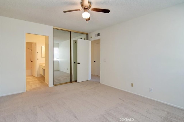 unfurnished bedroom with ceiling fan, light colored carpet, a closet, and connected bathroom