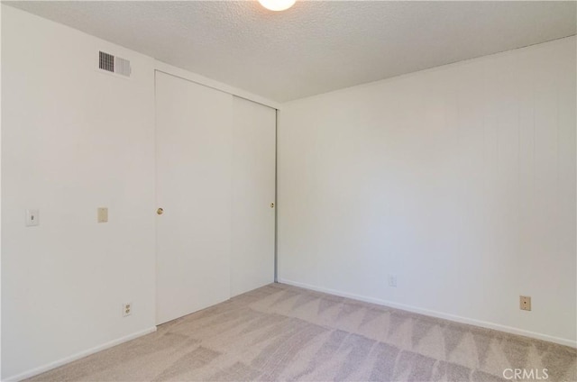 unfurnished bedroom with light colored carpet, a textured ceiling, and a closet