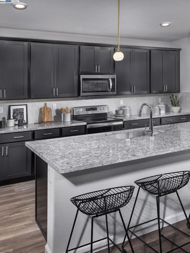 kitchen with sink, wood-type flooring, decorative light fixtures, a breakfast bar, and appliances with stainless steel finishes