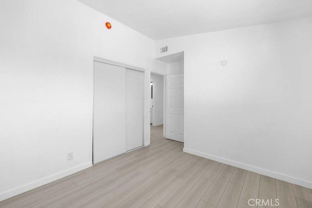 unfurnished bedroom with lofted ceiling, a closet, and light wood-type flooring