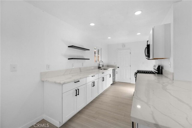 kitchen featuring light stone countertops, light wood-type flooring, white cabinetry, appliances with stainless steel finishes, and sink